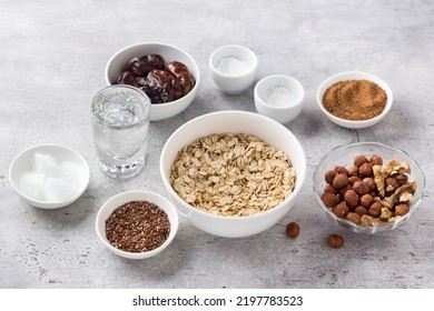 Ingredients For Cooking Healthy Oatmeal Cookies: Oatmeal, Flaxseed, Nuts (hazelnuts And Walnuts), Coconut Oil, Water, Dates, Coconut Sugar, Salt And Baking Powder On Gray Textured Background, Top View