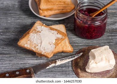 Ingredients for a delicious breakfast - toasted bread with butter and homemade raspberry jam on a wooden table.