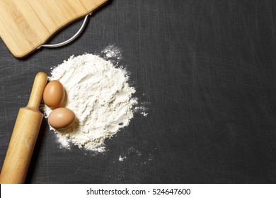 Ingredients for dough. Flour, eggs, rolling pin and cutting board on a black scratched background. Top view. Flat lay.