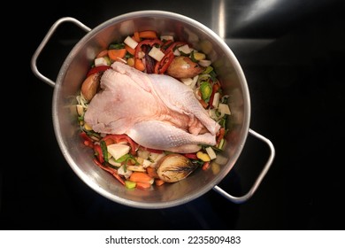 Ingredients for a healthy soup with a whole chicken and vegetables in a stainless-steel pot on the black stove, cooking for the immune system against cold and flu, top view from above, copy space - Powered by Shutterstock