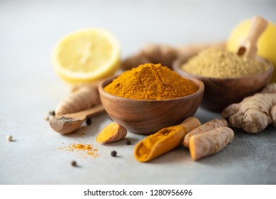 Ingredients for hot ayurvedic drink. Turmeric powder, curcuma root, cinnamon, ginger, lemon over grey background. Copy space, square crop. Spices for alternative medicine