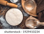 Ingredients for making bread. Active starter culture, flour, water on a brown wooden background.