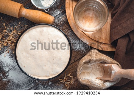 Ingredients for making bread. Active starter culture, flour, water on a brown wooden background.