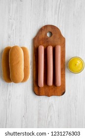 Ingredients For Making Hotdogs: Sausages On Wooden Board, Hot-dog Buns And Mustard On White Wooden Table, Top View. Flat Lay, Overhead, From Above.