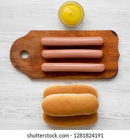 Ingredients For Making Hotdogs: Sausages On Rustic Wooden Board, Hot Dog Buns And Mustard On White Wooden Background, Top View. Flat Lay, Overhead, From Above.