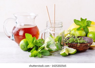 Ingredients For Making Ice Tea: Lemons, Limes, Mint And Glass Jar Over White Texture Background