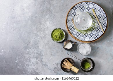 Ingredients For Making Matcha Ice Drink. Green Tea Matcha Powder In Ceramic Bowl, Traditional Bamboo Spoon, Whisk On Plate, Glass Teapot, Ice Cubes Over Grey Texture Background. Flat Lay, Space