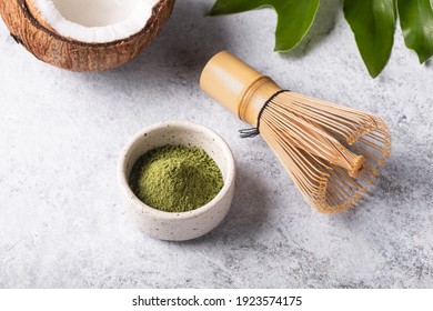 Ingredients for making matcha latte, Japanese green tea with coconut milk, traditional bamboo whisk chasen  on white concrete background close-up.