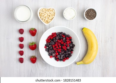 Ingredients For Making Smoothie Or Acai Bowl. Food Knolling. A Bowl With Acai, Stawberry, Raspberry, Banana, Chia Seeds, Coconut Flakes, Milk, Vegan Milk Or Yogurt. Flatlay, White Wooden Background.