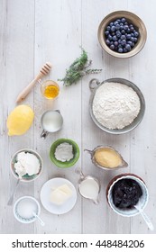 Ingredients Necessary To Prepare The Whole Wheat Blueberry Pancakes: Blueberries, Flour, Cornmeal, Lemon, Honey, Thyme, Butter, Blueberries Jam, Sugar, Milk, Buttermilk, Baking Powder. Flat Lay.