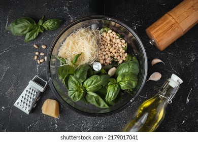 Ingredients For Pesto Sauce In The Blender Bowl. Green Basil Leaves, Parmesan Cheese And Pine Nuts On The Black Background. Flat Lay. Overhead View