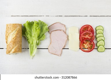 Ingredients For Sandwich: Lettuce, Bacon, Tomatoes, Cucumber, Cheese On A White Wooden Background