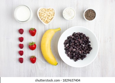 Ingredients For Smoothie Bowl. Food Knolling. A Bowl With Acai, Stawberry, Raspberry, Banana, Chia Seeds, Coconut Flakes, Milk, Vegan Milk Or Yogurt. Flatlay, White Wooden Background. Healthy Food.