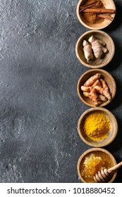 Ingredients for turmeric latte. Ground turmeric, curcuma root, cinnamon, ginger, honeycombs in wooden bowls in row over black texture background. Top view, copy space