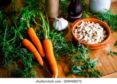 The Ingredients For A Vegan Green Pesto Made From Carrot Leaves Lie On A Large Wooden Table. Pepper, Olive Oil, Salt, Garlic And Cashew Nuts.