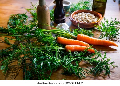 The Ingredients For A Vegan Green Pesto Made From Carrot Leaves Lie On A Large Wooden Table. Pepper, Olive Oil, Salt, Garlic And Cashew Nuts.