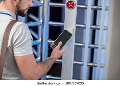 Ingress protection. Bearded young man applying smartphone to access scanner at turnstile of entrance organization