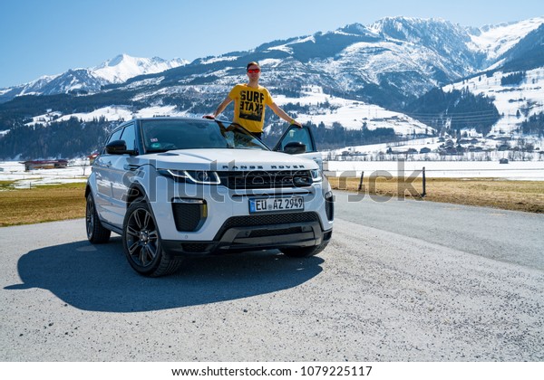 INGUS\
KRUKLITIS, WHITE RANGE ROVER EVUQUE. AUSTRIA, ALPS - MARCH 25,\
2018: Latest brand new white 2018 Range Rover Evoque parked by the\
mountains with a young man standing by the\
car.
