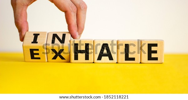 Inhale or exhale. Male hand flips
wooden cubes and changes the inscription 'exhale' to 'inhale' or
vice versa. Beautiful yellow table, white background, copy
space.