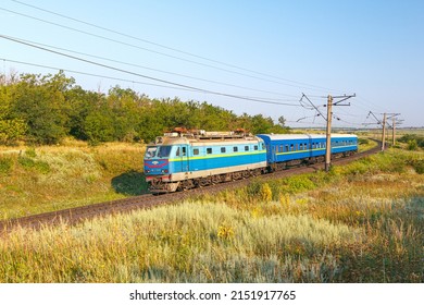 Inhulets, Ukraine - Summer 2021: Electric Locomotive Pulls Passenger Train Cars From Krivoy Rog To The Railway Station. Sunny Weather. Winding Road. Ukrainian Railway