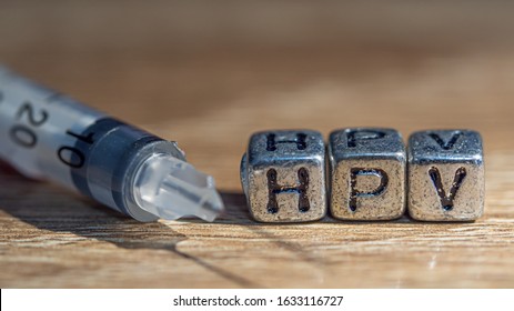 Injection needle with  Text " HPV"  put on wooden background. Concept Prevent HPV infection by vaccination before getting infected.