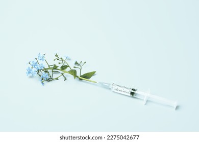 Injection syringe and flowers on blue background. Beauty Injections, vaccine creative concept. Healthcare and medical cosmetology.