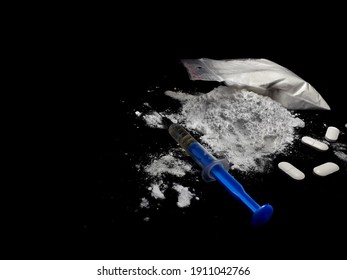 Injection syringe on the cocaine drug powder pile ang bag and pills on black background