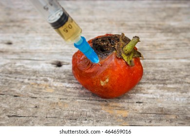 Injection of syringe in red missing tomato on wooden background. 