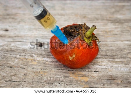 Injection of syringe in red missing tomato on wooden background. 