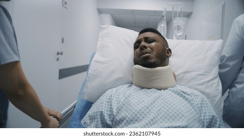 Injured African American man lies on gurney in neck brace and tries to talk with medics. Female doctor and nurse transport patient to hospital room. Medical staff at work in modern medical center. - Powered by Shutterstock