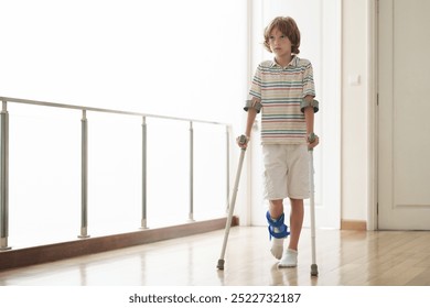 Injured child on crutches. Boy in cast on foot and leg. Little kid with sprained ancle learning to walk again. Physiotherapy in health clinic. Orthopedic trauma treatment. Doctor helping young patient - Powered by Shutterstock