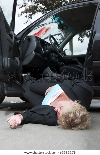 An\
injured driver with a severe head wound, lies unconsciously on the\
ground, fallen from her vehicle after an\
accident