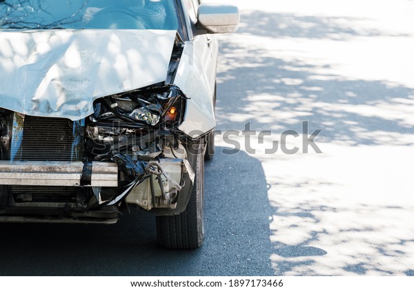Injured drunk man driving wrecked Destroyed\
car. Car crash traffic accident on city road. Smashed broken front\
auto headlight, dented hood without bumper on gray car. Auto life\
health insurance.
