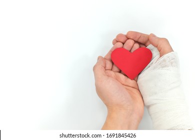 Injured Hands Holding Red Heart In White Background. Selfless Love, Sacrifice And Genuine Kindness Concept.