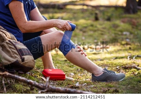 Injured hiker putting elastic bandage to her knee. Injury during hiking. First aid kit. Knee joint pain and tendon problems during adventure in nature