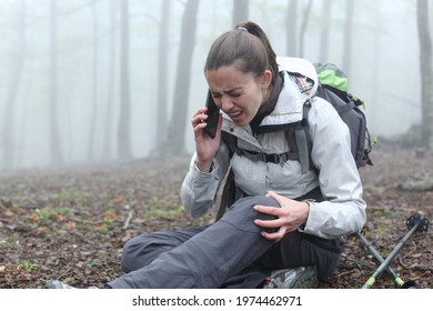 Injured hiker suffering knee fracture sitting on the ground asking for help calling on phone alone in a foggy forest - Shutterstock ID 1974462971
