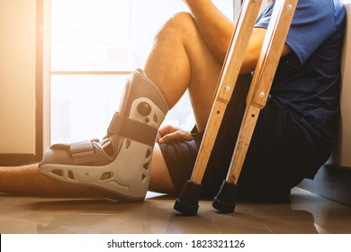injured man broken ankle wearing ankle support sitting in the house with soft-focus and  over light in the background