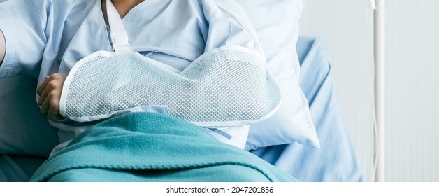 Injured Man Has Broken Arm In Cast  Lying On Hospital Bed. An Emergency Doctor First Aid Is Bandage And Hangs With Sling For Further Treatment In Orthopedic Clinic. Patient Pain From Accident Injury.