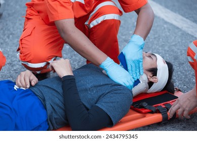 Injured man on patient transport stretcher. Ambulance staff member assisting injured person with transport stretcher. Paramedics assisting injured person first aid on road - Powered by Shutterstock