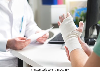 Injured patient showing doctor broken wrist and arm with bandage in hospital office or emergency room. Sprain, stress fracture or repetitive strain injury in hand. Nurse helping customer. First aid. - Shutterstock ID 788107459