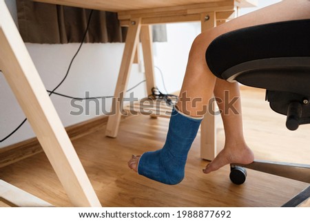 Injured woman of broken leg in plaster cast working at wooden desk