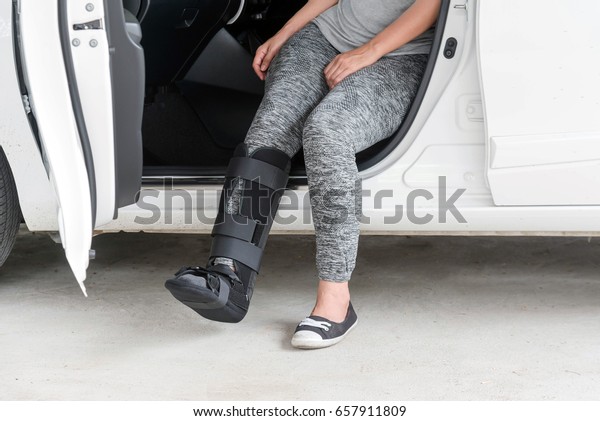 injured woman wearing sportswear\
with black cast on leg  sitting in white car, insurance\
concept.