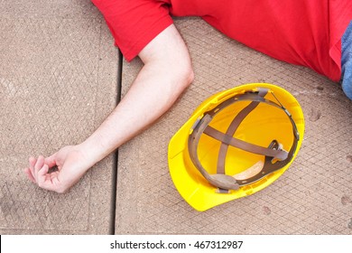Injured worker and hardhat on concrete surface.