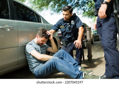 Injured Young Man Suffering In Pain After A Car Accident Talking With The Police Officers 