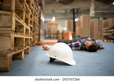 Injury At Work. Warehouse Worker Lying Unconscious On The Concrete Floor After The Fall. Focus On Hardhat.