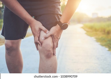 Verletzung durch das Konzept des Workout: Der Asiane benutzt Hände am Knie, während er im Park auf der Straße läuft. Morgenbespielen, Sonnenlicht und warmer Effekt mit Kopienraum für Text oder Design
