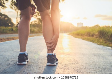 トレーニングのコンセプトによる損傷：そのアジア人の男性は公園で道路を走りながら足首を手でつかんでいる。足首に集中。
