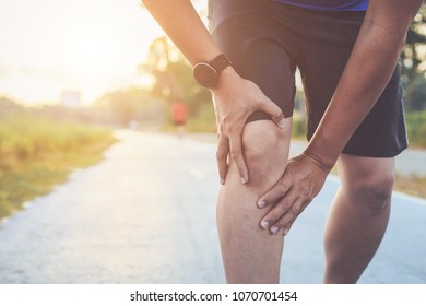 Injury from workout concept : The asian man use hands hold on his knee while running on road in the park. Shot in morning time, sunlight and warm effect with copy space for text or design - Shutterstock ID 1070701454