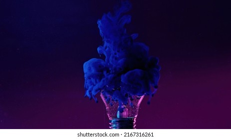 Ink water drop. Color smoke cloud. Fantasy imagination. Neon blue fluid in broken light bulb on purple gradient grain texture abstract art copy space background.