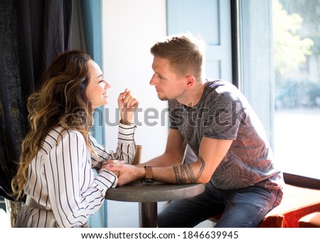inlove caucasian couple is sitting in cafe at a round table cups of coffee and are chatting each other near big panoramic window